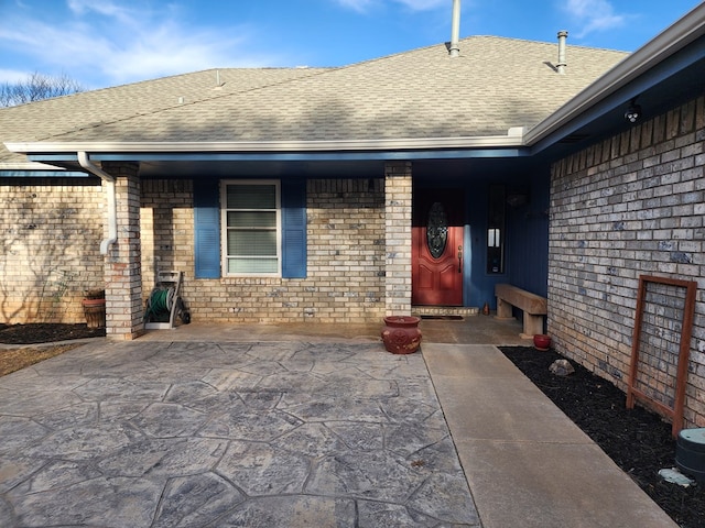 property entrance with a shingled roof and brick siding