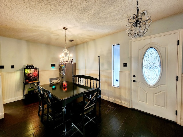 dining area with an inviting chandelier, a textured ceiling, dark wood-type flooring, and wainscoting