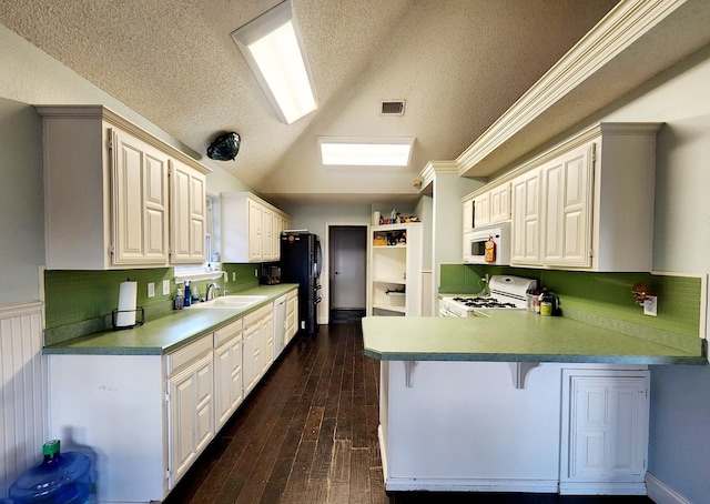 kitchen with dark wood-type flooring, vaulted ceiling, a sink, white appliances, and a peninsula