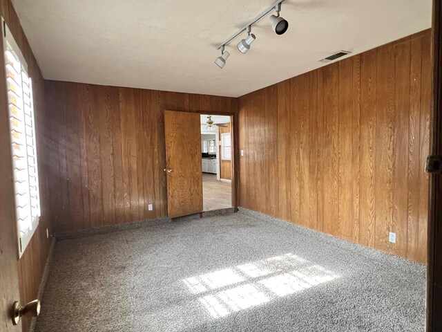 empty room featuring carpet floors, ceiling fan, wooden walls, and rail lighting