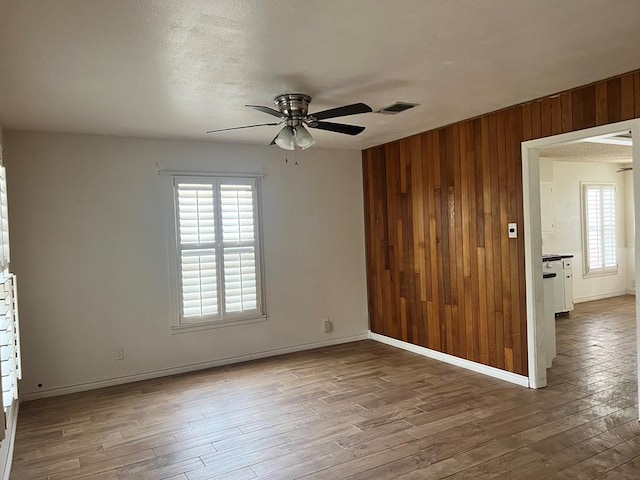 spare room with a textured ceiling, hardwood / wood-style flooring, ceiling fan, and wooden walls