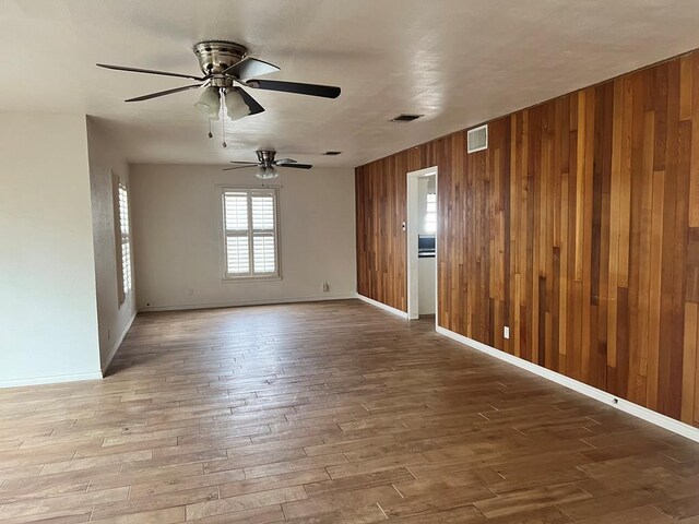 empty room featuring hardwood / wood-style flooring, ceiling fan, and wooden walls