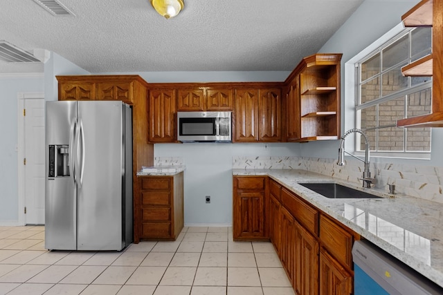 kitchen with sink, appliances with stainless steel finishes, light stone countertops, a textured ceiling, and light tile patterned flooring