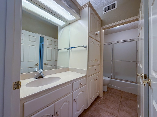 full bathroom featuring bath / shower combo with glass door, vanity, a textured ceiling, tile patterned floors, and toilet