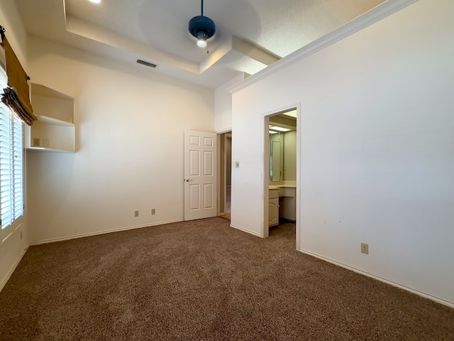 unfurnished bedroom featuring connected bathroom, a tray ceiling, and dark colored carpet