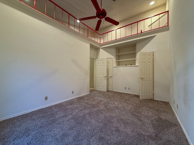 empty room with ceiling fan, carpet flooring, and a towering ceiling