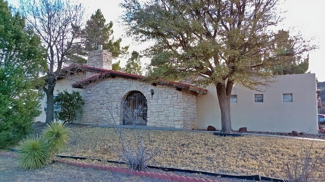 view of front facade with stone siding, a chimney, and stucco siding