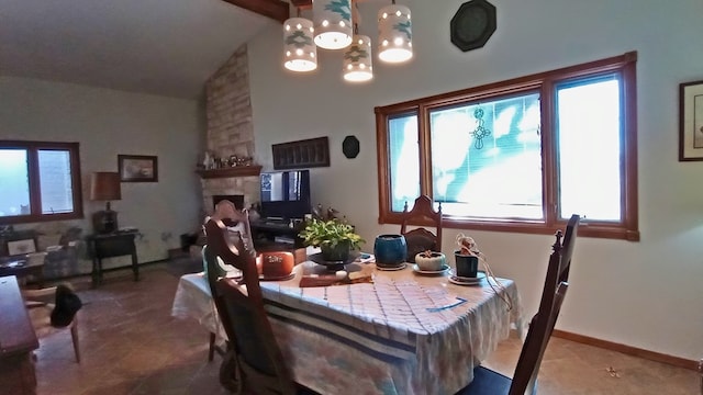 dining space with a chandelier, high vaulted ceiling, a stone fireplace, and baseboards