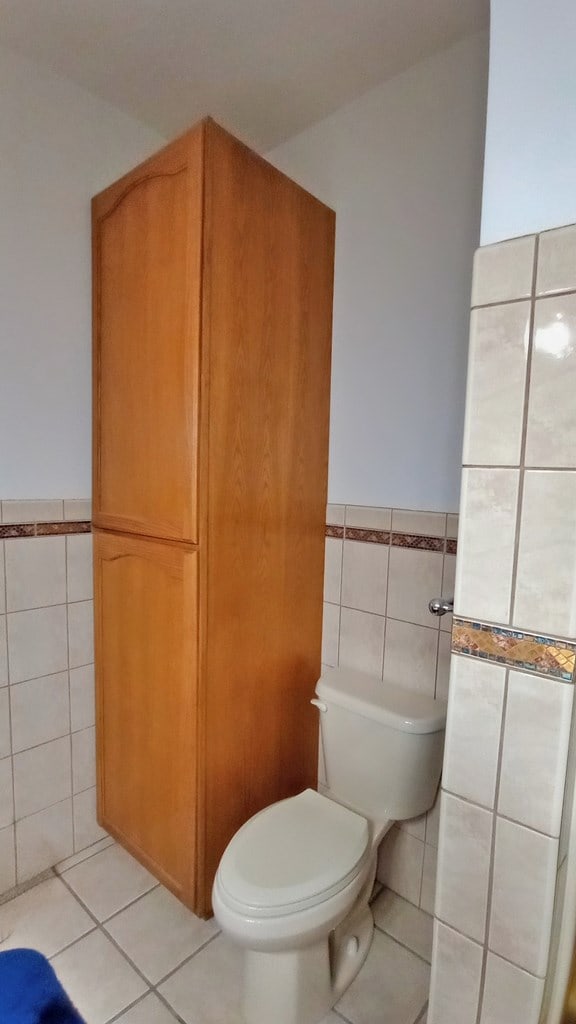 bathroom featuring toilet, a wainscoted wall, tile patterned flooring, and tile walls