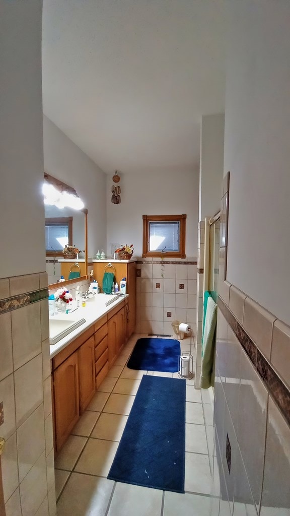 full bathroom featuring a wainscoted wall, tile patterned flooring, a shower, and tile walls