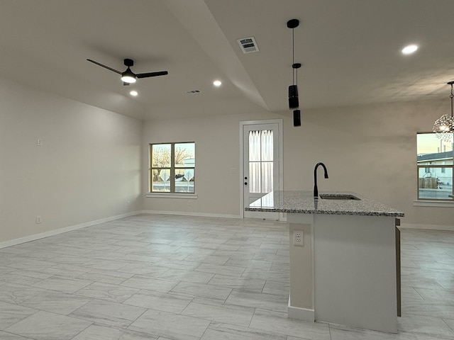 kitchen featuring sink, light stone countertops, a center island with sink, decorative light fixtures, and vaulted ceiling