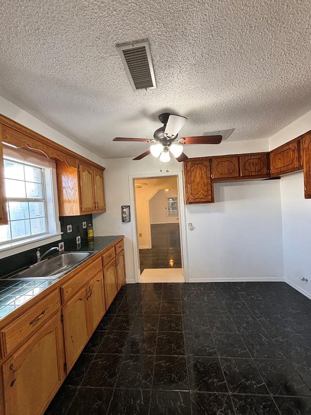 kitchen featuring tile countertops, sink, ceiling fan, decorative backsplash, and a textured ceiling