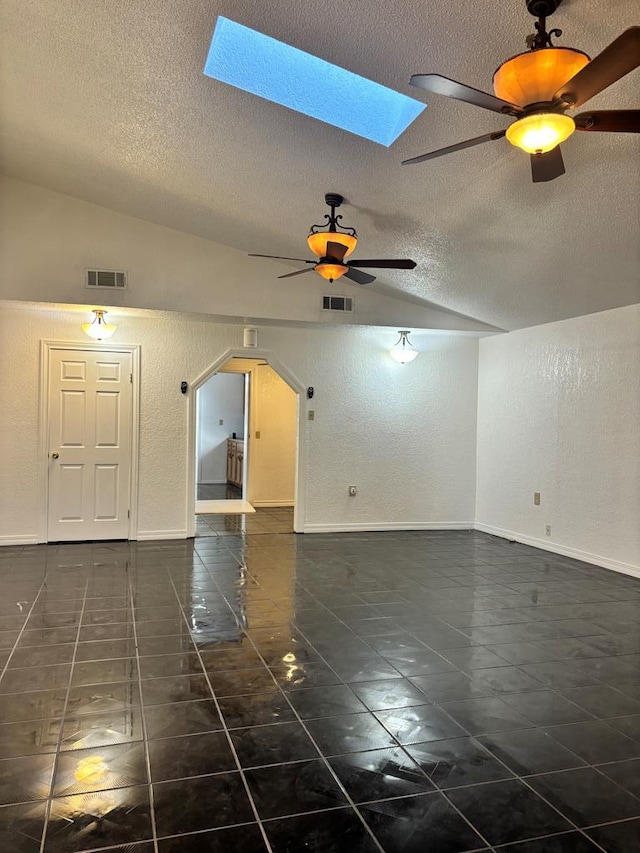 tiled empty room featuring a textured ceiling, ceiling fan, and vaulted ceiling with skylight