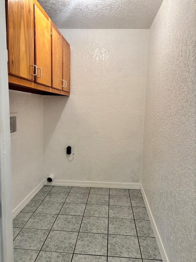 clothes washing area featuring light tile patterned floors, cabinets, and a textured ceiling