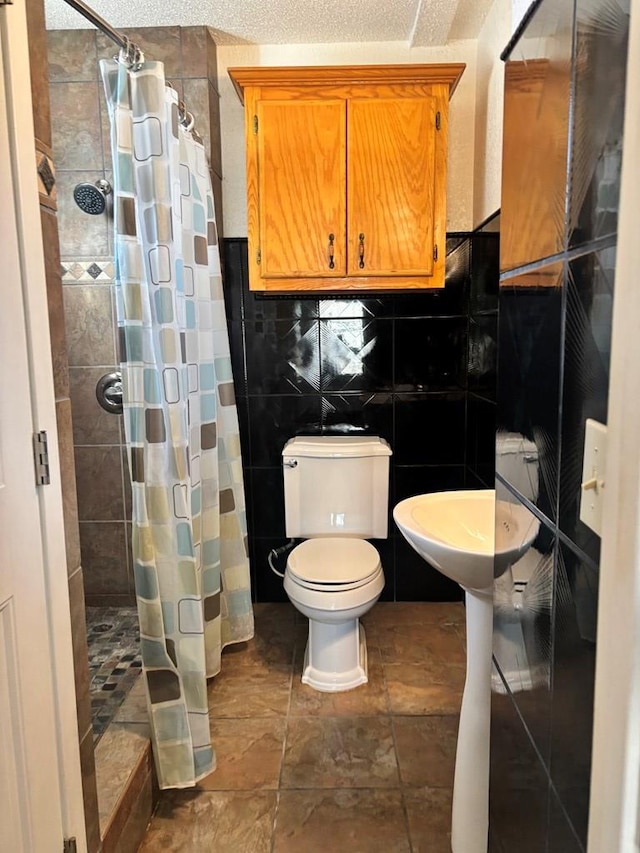 bathroom with a textured ceiling, toilet, tile walls, and a shower with shower curtain