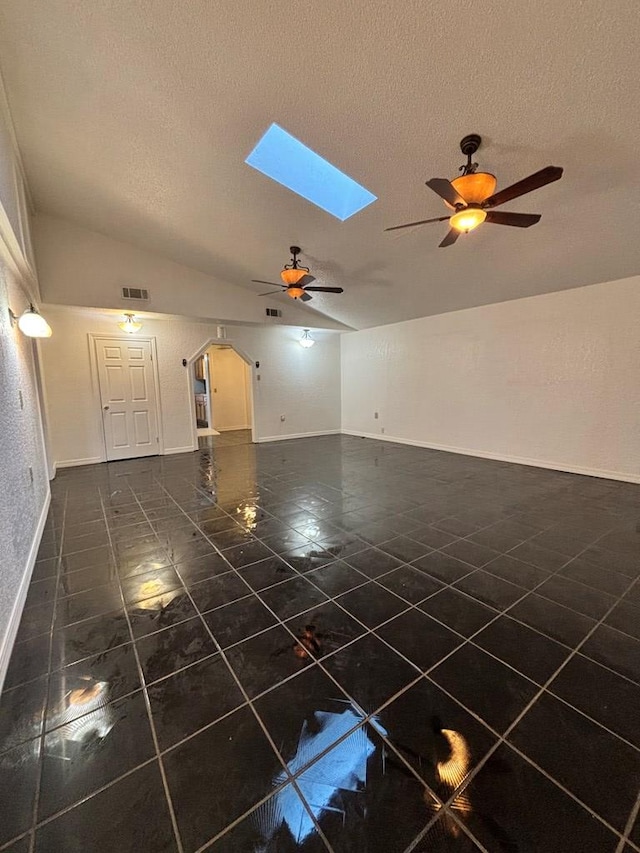 unfurnished living room featuring ceiling fan, vaulted ceiling with skylight, and a textured ceiling