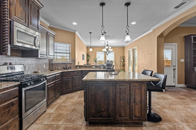 kitchen featuring a kitchen island, appliances with stainless steel finishes, decorative light fixtures, sink, and a kitchen bar