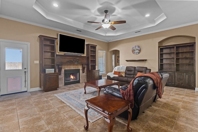 living room featuring ceiling fan, ornamental molding, a tray ceiling, and built in features