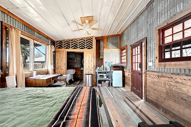 bedroom featuring ceiling fan, white fridge, light hardwood / wood-style floors, and wooden walls