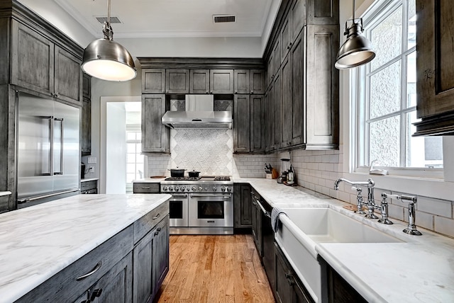 kitchen with pendant lighting, wall chimney exhaust hood, high quality appliances, and a wealth of natural light