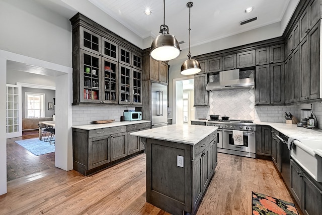 kitchen featuring a center island, decorative light fixtures, light wood-type flooring, premium appliances, and extractor fan