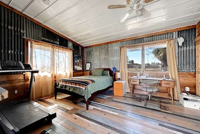 bedroom featuring ceiling fan, light hardwood / wood-style floors, and wooden walls