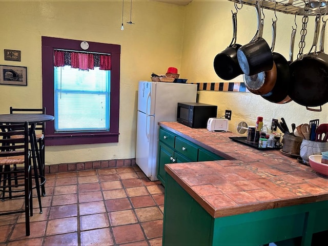 kitchen featuring tile patterned floors, tile countertops, and white fridge