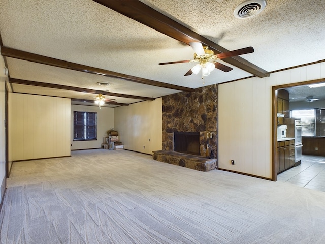 unfurnished living room featuring beam ceiling, a textured ceiling, light colored carpet, and a stone fireplace