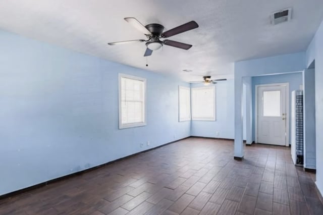 unfurnished room featuring visible vents, baseboards, dark wood-style floors, and a ceiling fan