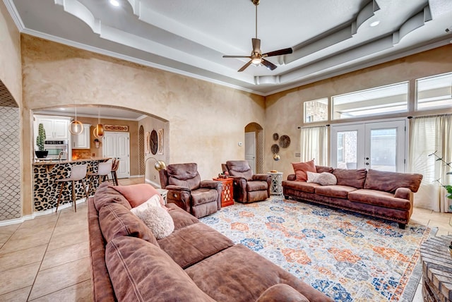 living area featuring a tray ceiling, light tile patterned floors, french doors, and arched walkways