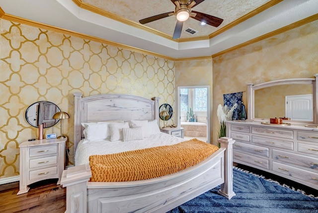 bedroom with a tray ceiling, dark wood-style floors, visible vents, and ornamental molding