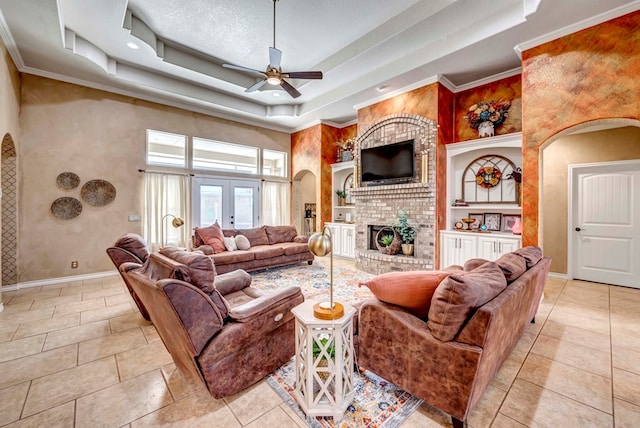 living room with built in shelves, baseboards, a tray ceiling, arched walkways, and a brick fireplace