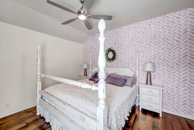 bedroom with dark wood finished floors, an accent wall, baseboards, and vaulted ceiling