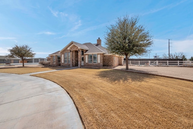 view of front of house with brick siding, a chimney, a front yard, and fence