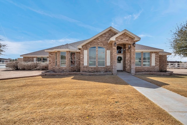 view of front of home with brick siding, a shingled roof, and a front lawn