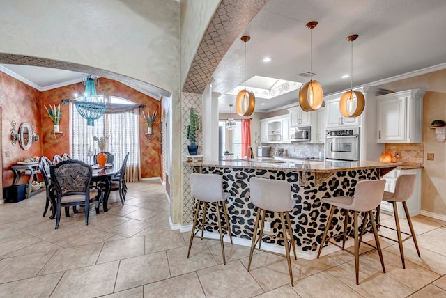 kitchen featuring ornamental molding, appliances with stainless steel finishes, a breakfast bar area, white cabinets, and a chandelier