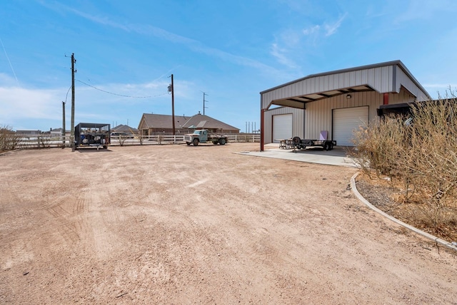 view of yard featuring a detached garage, an outbuilding, dirt driveway, and fence