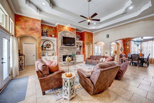 living room featuring a raised ceiling, a brick fireplace, visible vents, and arched walkways