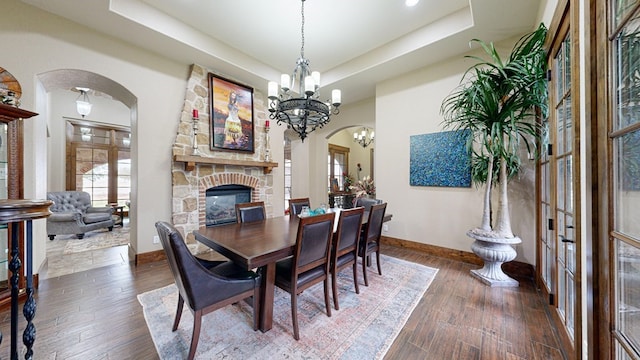 dining room featuring an inviting chandelier, dark hardwood / wood-style floors, a raised ceiling, and a stone fireplace