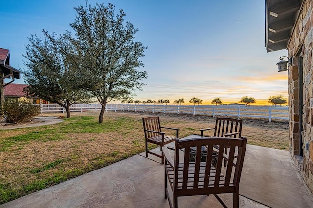 patio terrace at dusk featuring a lawn and a rural view