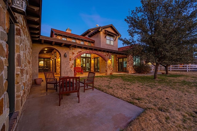 back house at dusk with a patio and a lawn