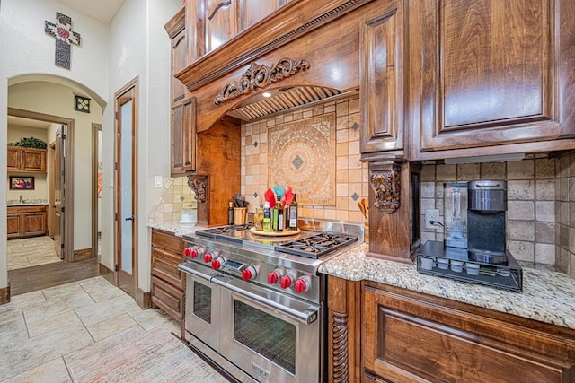 kitchen with sink, premium range hood, light stone counters, decorative backsplash, and range with two ovens