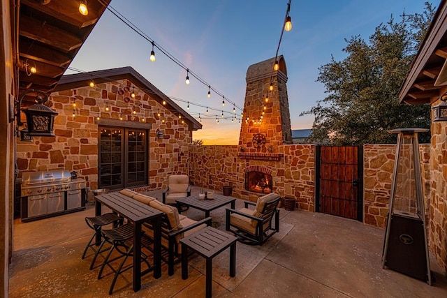 patio terrace at dusk featuring a grill and an outdoor stone fireplace