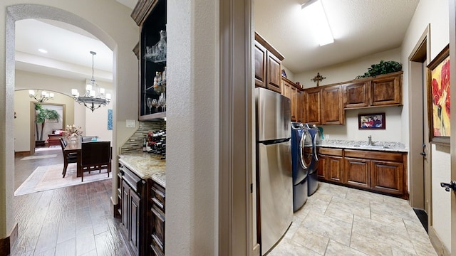 kitchen with sink, decorative light fixtures, stainless steel fridge, light stone countertops, and washing machine and dryer