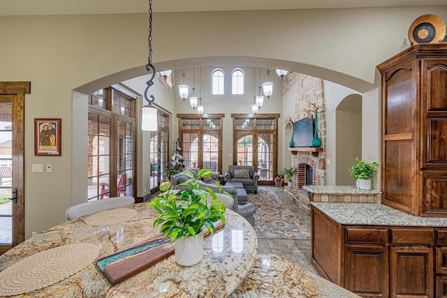 kitchen with hanging light fixtures, a high ceiling, light stone counters, a stone fireplace, and french doors