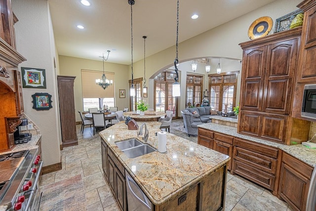 kitchen with sink, stainless steel appliances, light stone counters, an island with sink, and decorative light fixtures