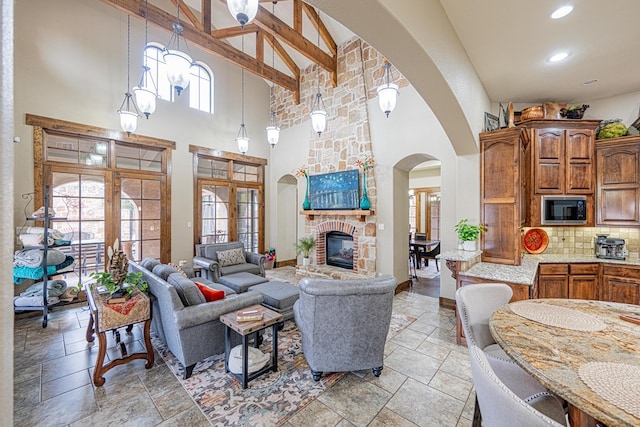 living room featuring beamed ceiling, a fireplace, a high ceiling, and a wealth of natural light