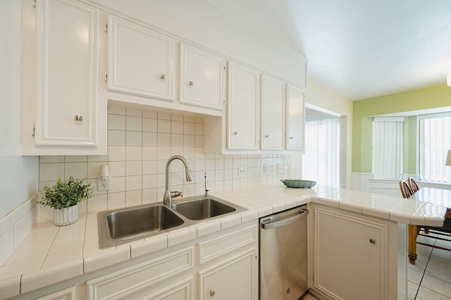 kitchen with white cabinetry, stainless steel dishwasher, tile counters, and sink