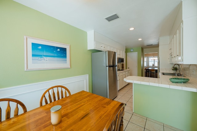 kitchen featuring sink, stainless steel fridge, white cabinetry, tile counters, and light tile patterned flooring