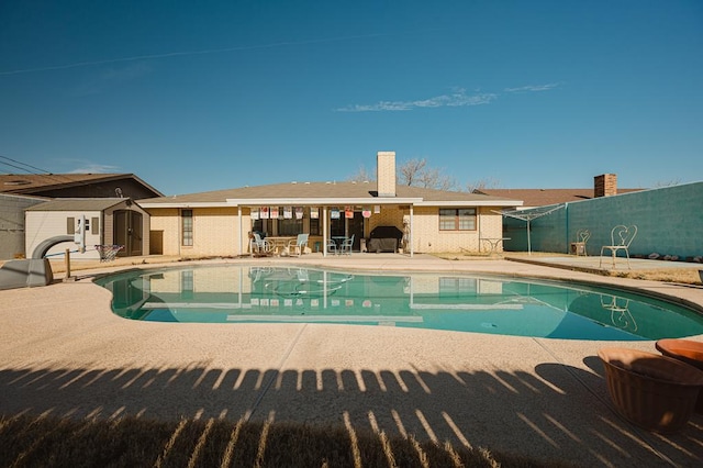 view of swimming pool featuring a patio and a storage shed